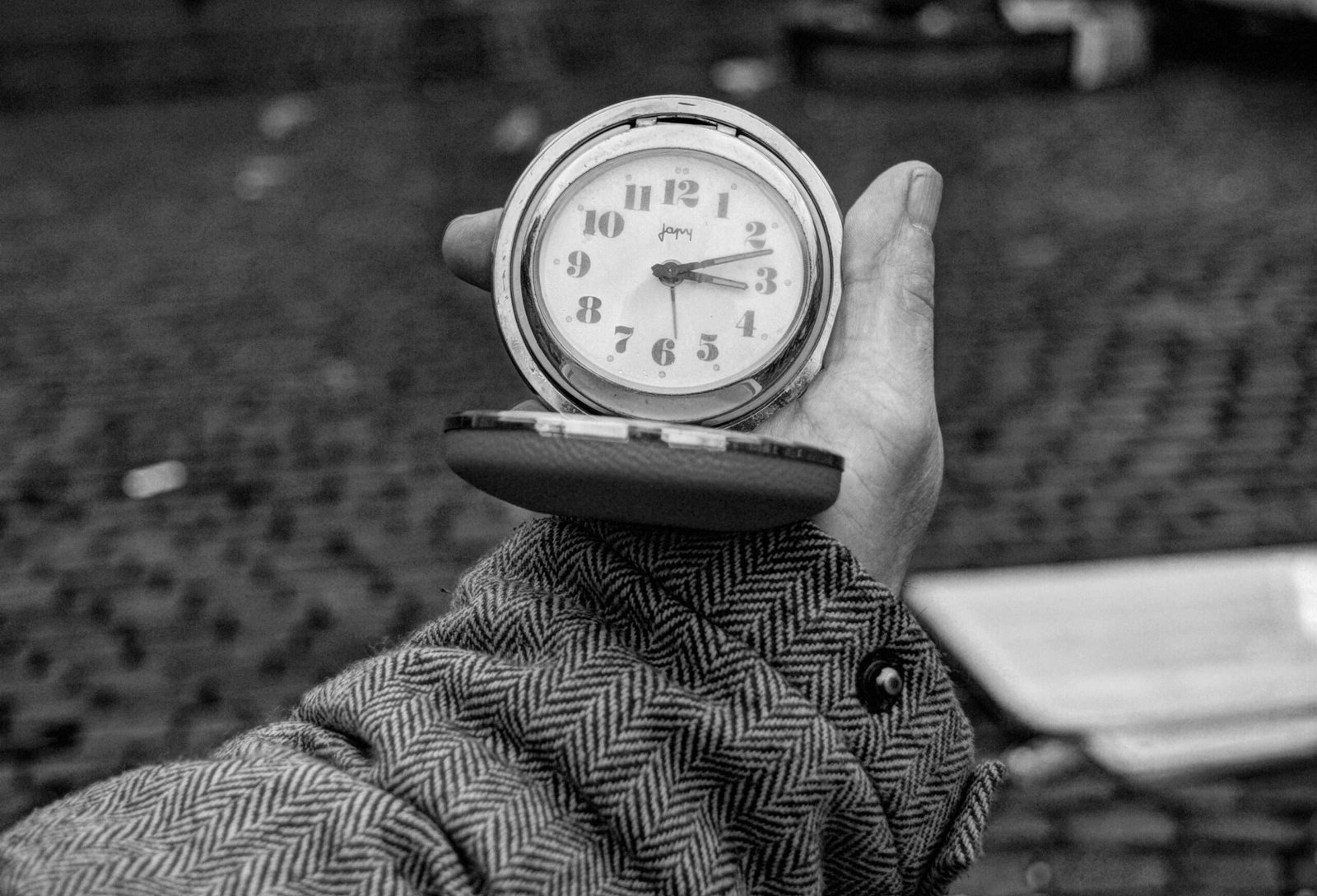 A photo of a man holding an alarm clock he found on the street after a flea market. It was then effectively thirteen minutes past three, that clock still worked.