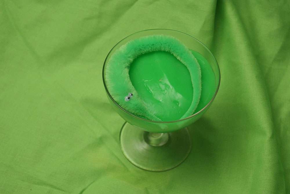 A little green monster in a champagne glass full of slime.