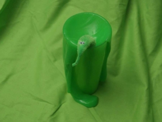 A little green monster escapes from a cup full of green slime.