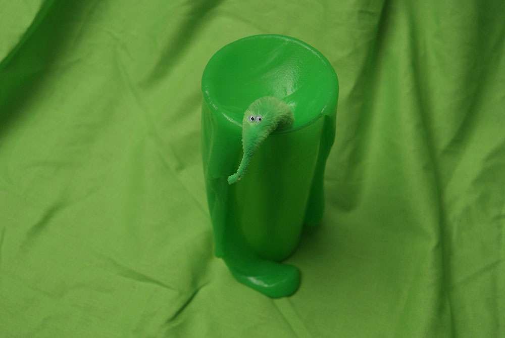 A little green monster escapes from a cup full of green slime.