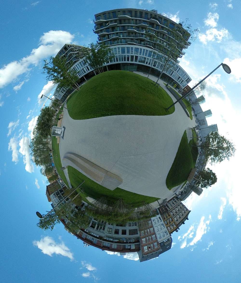 This Tiny Planet is a view of the Schengenplein, a new square in the so called Cadix district of Antwerp, that officially opened in June 2017. The green square is located on the former car park of the former customs building, is completely car-free, and also contains various play areas for children and rest areas. It crosses the Kattendijkdok-Oostkaai, where a tram also runs, so that you can reach the square from the center of the city in just ten minutes.